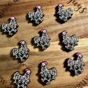 Nine decorated cookies shaped like chickens wearing Christmas lights and Santa hats are arranged on a wooden board.