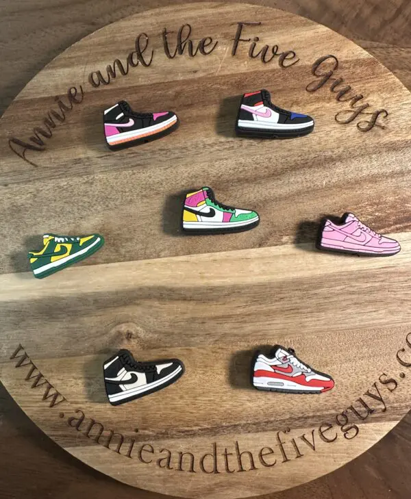 Wooden board with text, displaying seven small, colorful sneaker-shaped pins.