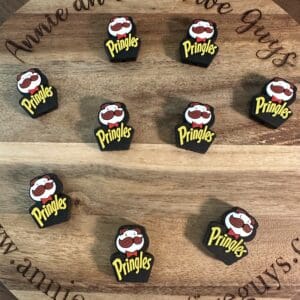 Nine black Pringles-themed guitar picks arranged on a round wooden surface with decorative text around the edge.