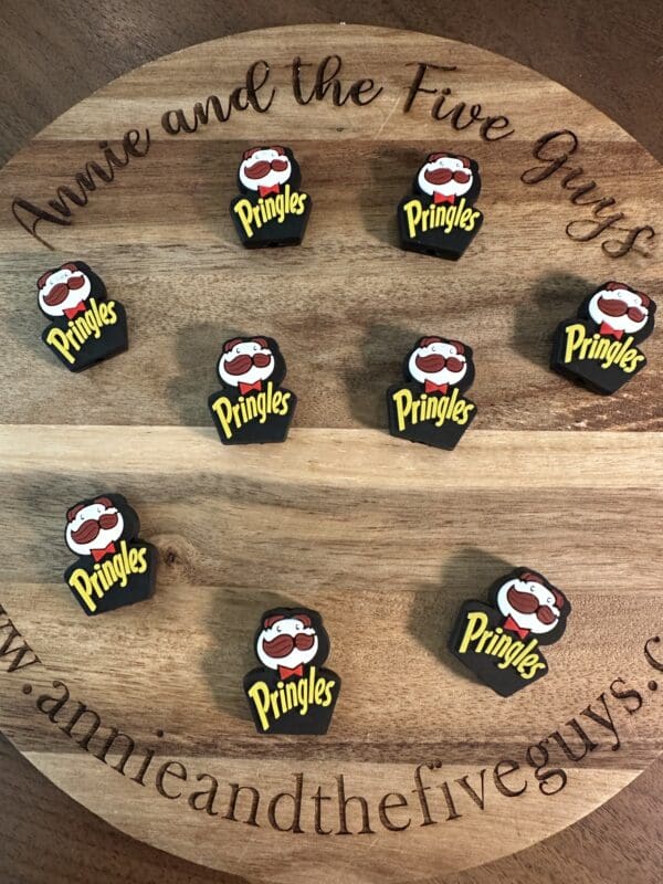 Nine black Pringles-themed guitar picks arranged on a round wooden surface with decorative text around the edge.