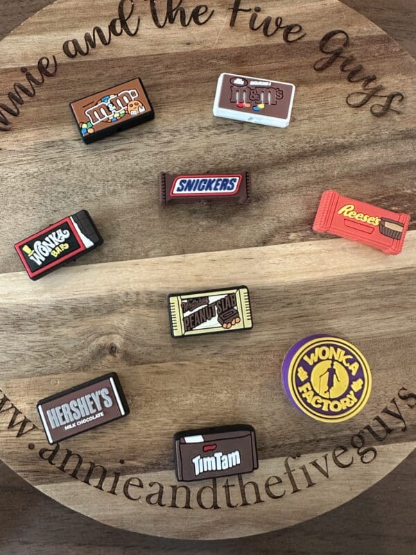 Assorted candy-themed magnets, including M&M's, Snickers, Reese's, Hershey's, and more, are displayed on a wooden surface.