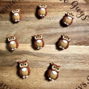 Nine owl-shaped cookies are arranged on a round wooden board with engraved text along the edges.