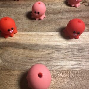 Small pink and red rubber octopus toys are placed on a wooden surface.