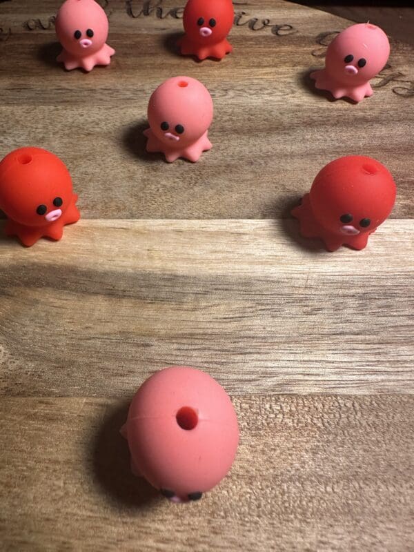 Small pink and red rubber octopus toys are placed on a wooden surface.