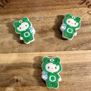 Two cookies shaped like cartoon characters in green bear costumes with milk bottles, displayed on a wooden surface.