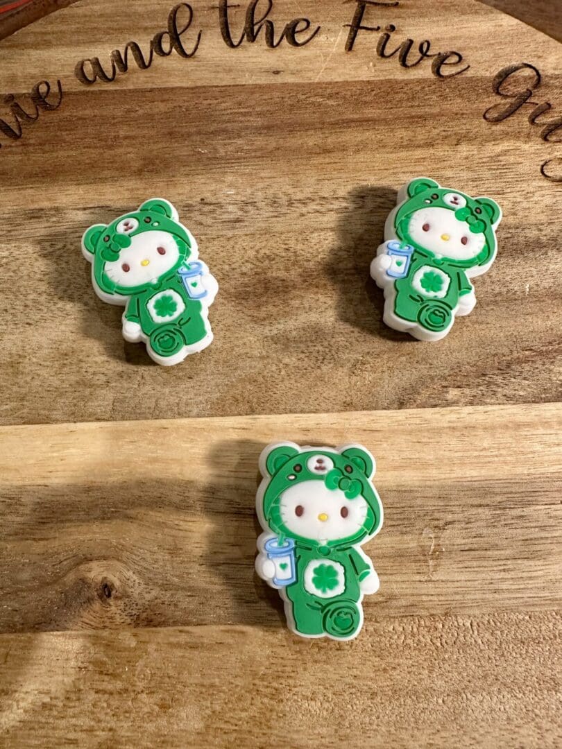 Two cookies shaped like cartoon characters in green bear costumes with milk bottles, displayed on a wooden surface.