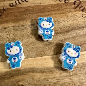 Three cookies shaped like a cartoon character wearing a blue bear onesie and holding a nurse badge, placed on a wooden surface.