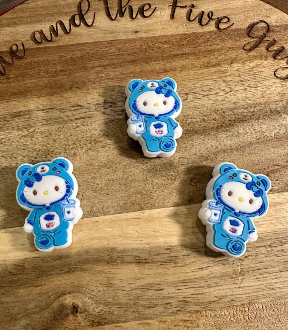 Three cookies shaped like a cartoon character wearing a blue bear onesie and holding a nurse badge, placed on a wooden surface.