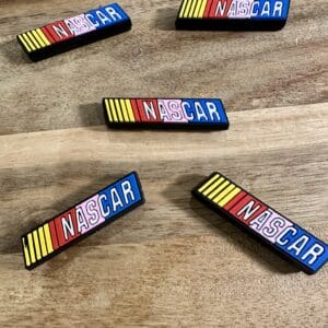 Five rectangular NASCAR logo magnets with colorful stripes are spread on a wooden surface.