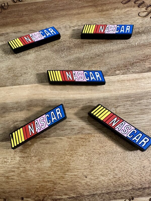 Five rectangular NASCAR logo magnets with colorful stripes are spread on a wooden surface.