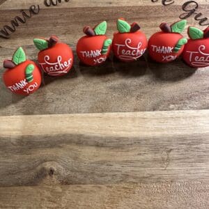 Five red apple-shaped ornaments with "Thank You" and "Teacher" written on them are displayed on a wooden surface with "Annie and the Five Guys" engraved above.