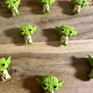 Nine small Yoda figurines are arranged in a grid on a wooden surface.