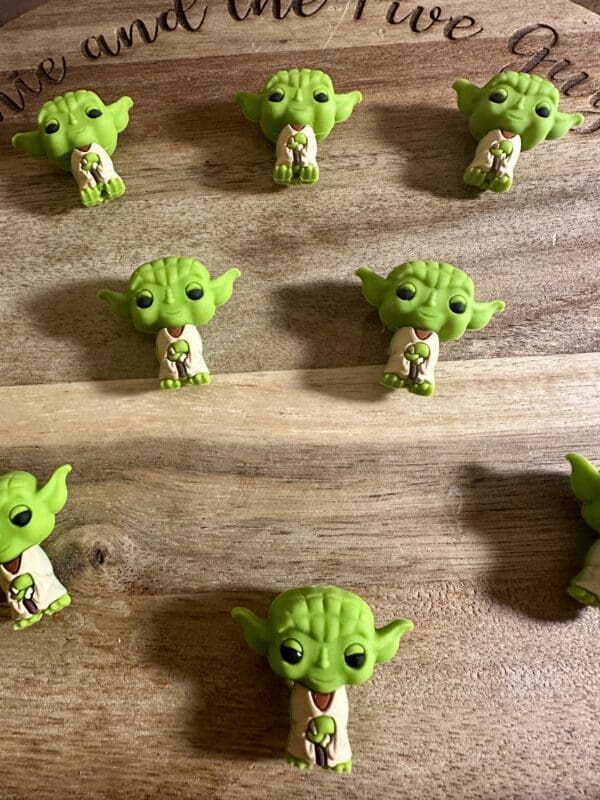 Nine small Yoda figurines are arranged in a grid on a wooden surface.